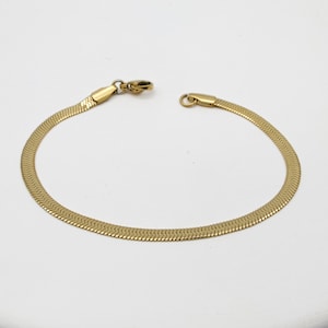 Könnte beinhalten: Ein goldfarbenes Schlangenkettenarmband mit einem Verschluss.