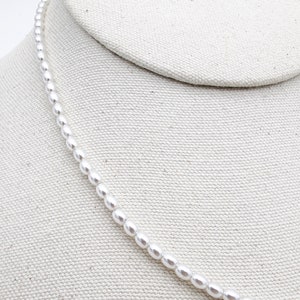 May include: A white pearl necklace displayed on a white fabric background.