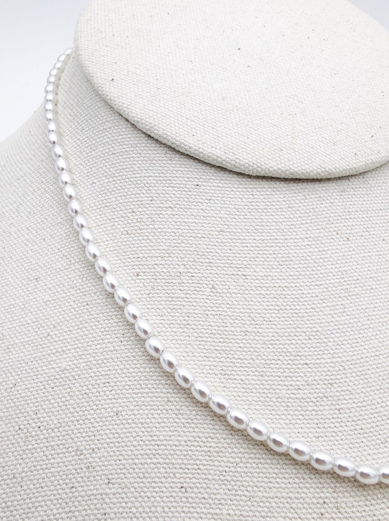 May include: A white pearl necklace displayed on a white fabric background.