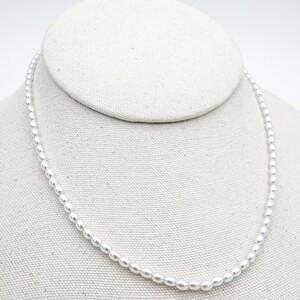 May include: A simple white pearl necklace displayed on a white fabric mannequin bust.