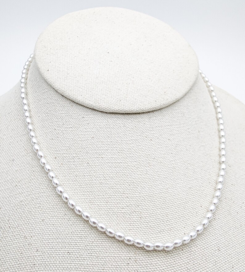 May include: A simple white pearl necklace displayed on a white fabric mannequin bust.