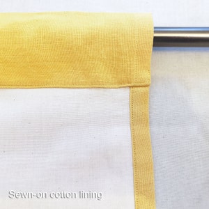 May include: Close-up of a yellow cotton lining sewn onto a white fabric curtain. The lining is visible along the top edge and the side edge of the curtain.