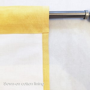 May include: A white curtain with a yellow cotton lining. The curtain is hung on a metal rod.