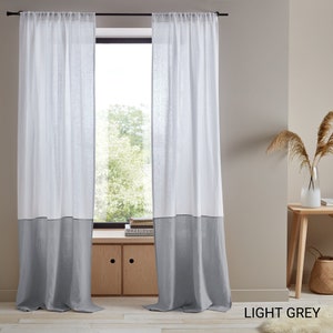 May include: Two sheer white linen curtains with a light gray bottom panel. The curtains are hung on a black curtain rod. The curtains are in front of a window with a view of trees. The text "LIGHT GREY" is in the bottom right corner of the image.