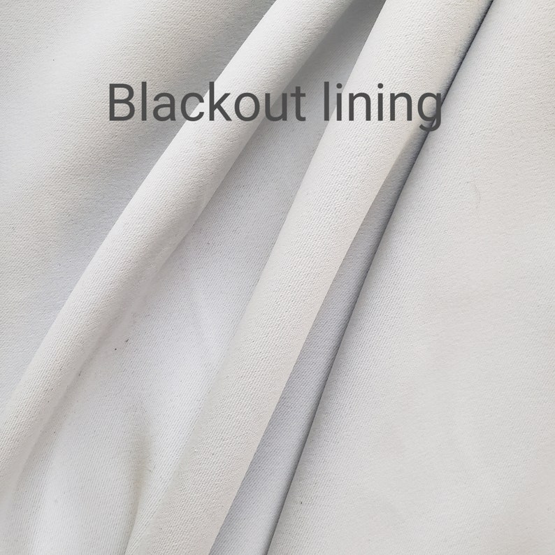 May include: Close-up of white fabric with a smooth texture. The fabric is folded in half, and the words "Blackout lining" are printed on the top fold.