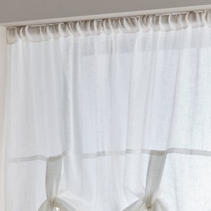 May include: White sheer curtains with a gathered top and a decorative tie-back detail. The curtains are hung on a white rod.
