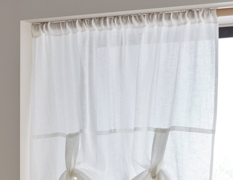 May include: White sheer curtains with a gathered top and a decorative tie-back detail. The curtains are hung on a white rod.