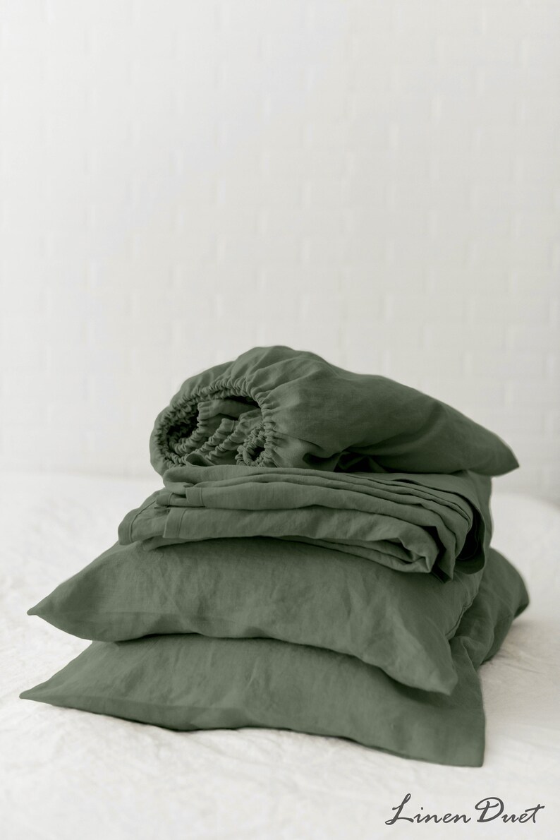 May include: A stack of sage green linen bedding, including a fitted sheet, flat sheet, and pillowcases. The bedding is folded neatly and arranged on a white surface. The text "Linen Duet" is visible in the bottom right corner of the image.