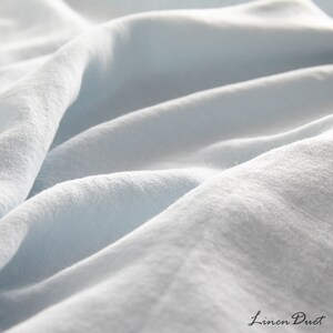 May include: Close-up of a light blue linen fabric with a soft, textured surface. The fabric is wrinkled and folded, creating a sense of comfort and relaxation.