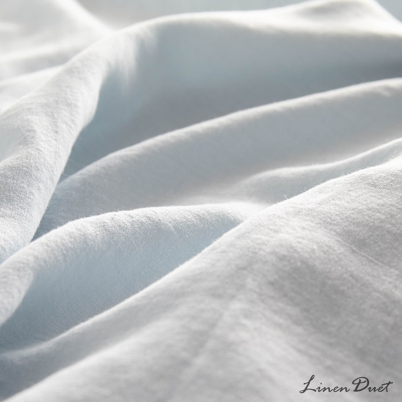 May include: Close-up of a light blue linen fabric with a soft, textured surface. The fabric is wrinkled and folded, creating a sense of comfort and relaxation.