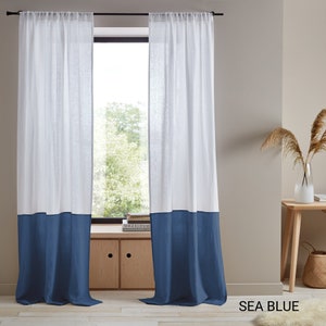 May include: White linen curtains with a blue bottom border. The curtains are hung on a black rod and are in front of a window with a view of trees. The text "SEA BLUE" is visible in the bottom right corner of the image.