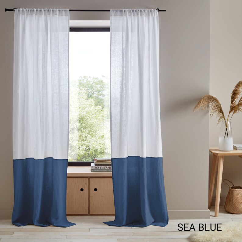 May include: White linen curtains with a blue bottom border. The curtains are hung on a black rod and are in front of a window with a view of trees. The text "SEA BLUE" is visible in the bottom right corner of the image.