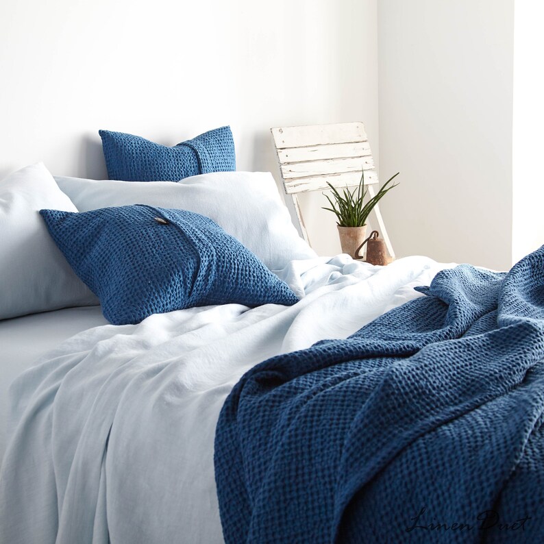 May include: A blue waffle weave throw blanket on a bed with blue waffle weave pillow covers and white linen sheets.