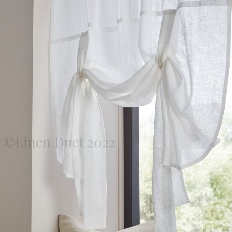 May include: White sheer linen tie-top window valance with a gathered and tied design. The valance is made of a lightweight fabric and has a simple, elegant look.