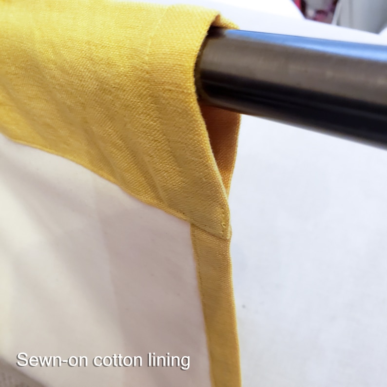 May include: Close-up of a yellow cotton lining sewn onto a white fabric panel. The fabric is hanging from a metal rod.