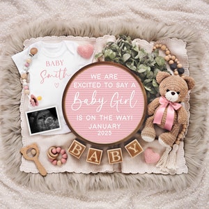 K&ouml;nnte beinhalten: Ein rosa-wei&szlig;es Baby-Ank&uuml;ndigungs-Schild mit dem Text "We are excited to say a Baby Girl is on the way! January 2025". Das Schild ist umgeben von einem wei&szlig;en Strampler mit dem Text "Baby Smith", einem Teddyb&auml;r und Holzkl&ouml;tzen, die "Baby" buchstabieren.