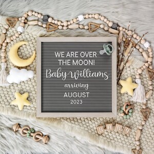 Peut inclure: Un tableau d'affichage en lettres grises avec le texte "We are over the moon! Baby Williams arriving August 2023". Le tableau est entour&eacute; de perles en bois, d'une sucette, d'une &eacute;toile en bois et d'autres d&eacute;corations sur le th&egrave;me des b&eacute;b&eacute;s.