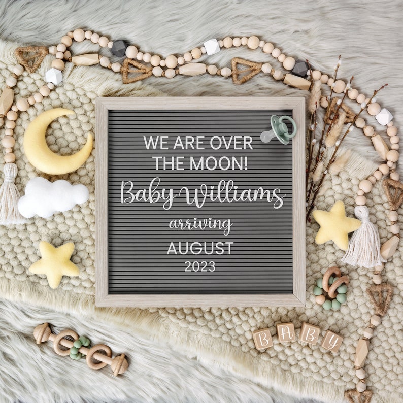 Peut inclure: Un tableau d'affichage en lettres grises avec le texte "We are over the moon! Baby Williams arriving August 2023". Le tableau est entour&eacute; de perles en bois, d'une sucette, d'une &eacute;toile en bois et d'autres d&eacute;corations sur le th&egrave;me des b&eacute;b&eacute;s.