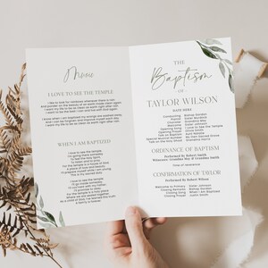 May include: A baptism program with the text "The Baptism of Taylor Wilson" in elegant script. The program includes details of the ceremony, with floral accents. The program is held open, revealing the inside pages.