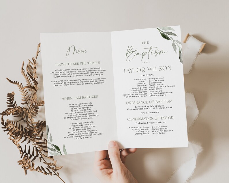 May include: A baptism program with the text "The Baptism of Taylor Wilson" in elegant script. The program includes details of the ceremony, with floral accents. The program is held open, revealing the inside pages.