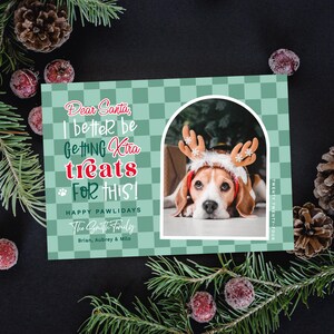 May include: A holiday greeting card with a beagle wearing reindeer antlers. The card has a green checkered pattern and text that reads "Dear Santa, I better be getting extra treats for this!" and "Happy Pawlidays."