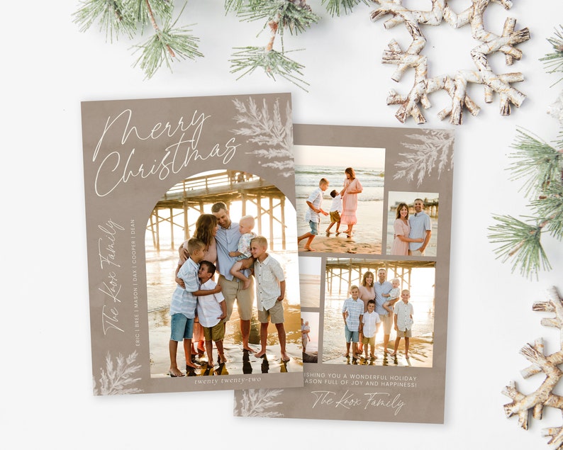 May include: A Christmas card featuring a family of five on a beach with a pier in the background. The card is decorated with a white, brushstroke design and the text "Merry Christmas" and "The Fox Family".
