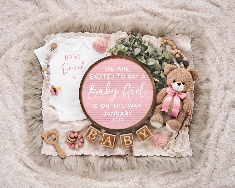K&ouml;nnte beinhalten: Ein rosa-wei&szlig;es Buchstabenbrett mit dem Text "We are excited to say a Baby Girl is on the way! January 2025". Das Buchstabenbrett ist umgeben von einem wei&szlig;en Strampler mit dem Text "Baby Oneil", einem rosa-wei&szlig;en Teddyb&auml;r und Holzbl&ouml;cken, die "BABY" buchstabieren.