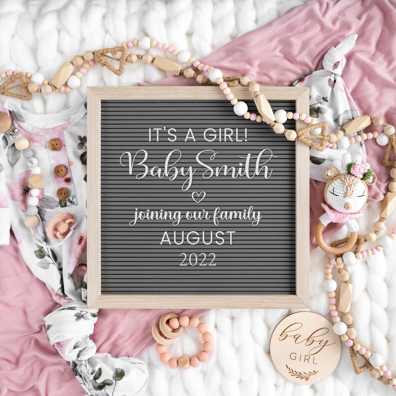 Może przedstawiać: Szara tablica z literami z tekstem "It's a girl! Baby Smith joining our family August 2022". Tablica jest otoczona r&oacute;żowymi i białymi koralikami, r&oacute;żowym i białym ubraniem dla dziecka, drewnianą grzechotką dla dziecka i drewnianym znakiem z napisem "baby girl".