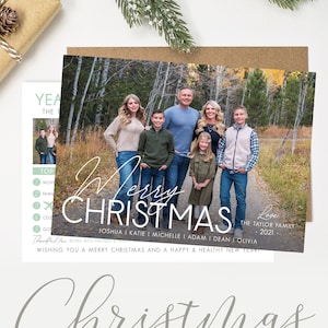May include: A Christmas card template featuring a family of seven standing on a path in a forest. The card has a white background with the text "Merry Christmas" in a bold, white font. The text "Love, The Taylor Family 2021" is in a smaller, white font below the main text. The card also includes the text "Wishing you a Merry Christmas and a Happy & Healthy New Year!" in a smaller, white font at the bottom.