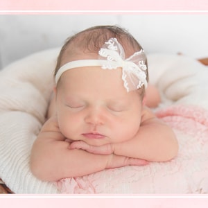 K&ouml;nnte beinhalten: Ein schlafendes Baby M&auml;dchen, das ein wei&szlig;es Stirnband mit einer Schleife aus Spitze tr&auml;gt, liegt auf einer wei&szlig;en und rosa Decke.