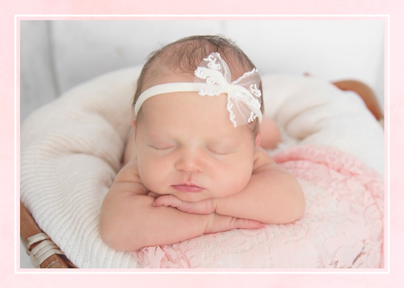 K&ouml;nnte beinhalten: Ein schlafendes Baby M&auml;dchen, das ein wei&szlig;es Stirnband mit einer Schleife aus Spitze tr&auml;gt, liegt auf einer wei&szlig;en und rosa Decke.