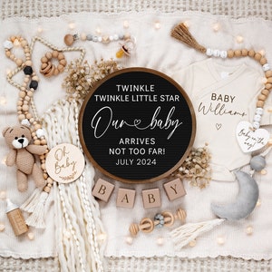 May include: A wooden sign with the text "Twinkle Twinkle Little Star Our Baby Arrives Not Too Far! July 2024" surrounded by a white blanket, a wooden baby rattle, a wooden baby bottle, a crocheted teddy bear, a white onesie with the text "Baby Williams" and a wooden heart with the text "Baby on the way".