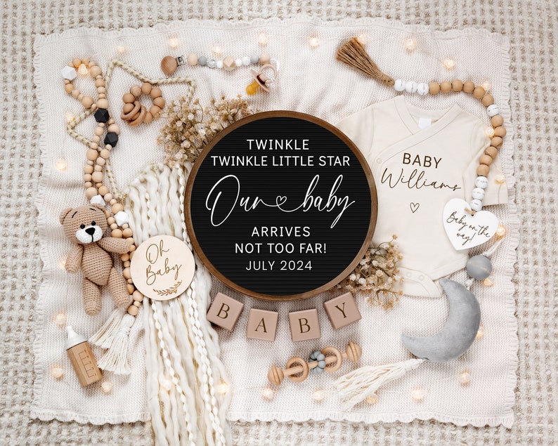 May include: A wooden sign with the text "Twinkle Twinkle Little Star Our Baby Arrives Not Too Far! July 2024" surrounded by a white blanket, a wooden baby rattle, a wooden baby bottle, a crocheted teddy bear, a white onesie with the text "Baby Williams" and a wooden heart with the text "Baby on the way".