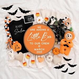 May include: A Halloween-themed baby announcement with a round orange sign that reads "We are adding a little boo to our crew, March 2025". The sign is surrounded by a black and white beaded garland, a black onesie with the text "Baby Salem", a white ghost, a pumpkin-shaped stuffed animal, and other Halloween decorations.