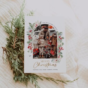 May include: A Christmas card featuring a family of four standing in front of a car. The card has a watercolor border with red berries and green leaves. The text "THE WILLIAMS FAMILY" is at the top of the card, and the text "MERRY Christmas" is at the bottom. The year "24" is also included. The names of the family members are listed below the greeting: "matthew. lacy, hazel, isabella. mickey"