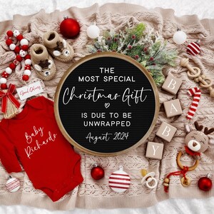Pu&ograve; includere: Un body rosso per neonato con il testo "Baby Richards" in bianco. Una lavagna con lettere nere con il testo "The Most Special Christmas Gift is Due to Be Unwrapped August 2024". Il body e la lavagna con lettere sono circondati da decorazioni natalizie, tra cui una canna di zucchero, ornamenti e un giocattolo di renna.