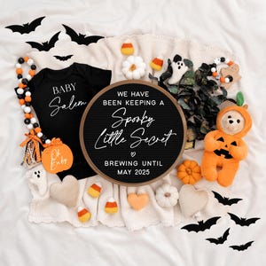 Puede incluir: Un tablero de letras negro con el texto "We have been keeping a Spooky Little Secret ♡ Brewing until May 2025". El tablero est&aacute; rodeado de decoraciones de Halloween, incluyendo un body negro con el texto "Baby Salem", un juguete de peluche con forma de calabaza y un oso de peluche con un disfraz de calabaza.