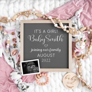 Może przedstawiać: Szara tablica z literami z tekstem "It's a girl! Baby Smith joining our family August 2022". Widoczne są zdjęcie USG, drewniany napis "baby girl" oraz r&oacute;żowo-biały str&oacute;j dla dziecka z kwiatowym wzorem.