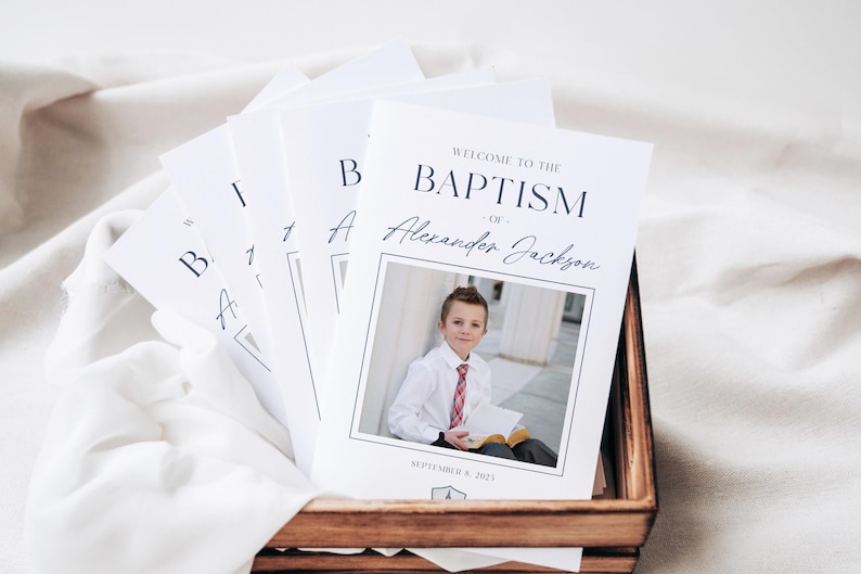 May include: White and black program for a baptism ceremony. The program features a photo of a young boy in a white shirt and red tie, holding a book. The text reads "Welcome to the Baptism of Alexander Jackson, September 9, 2023".