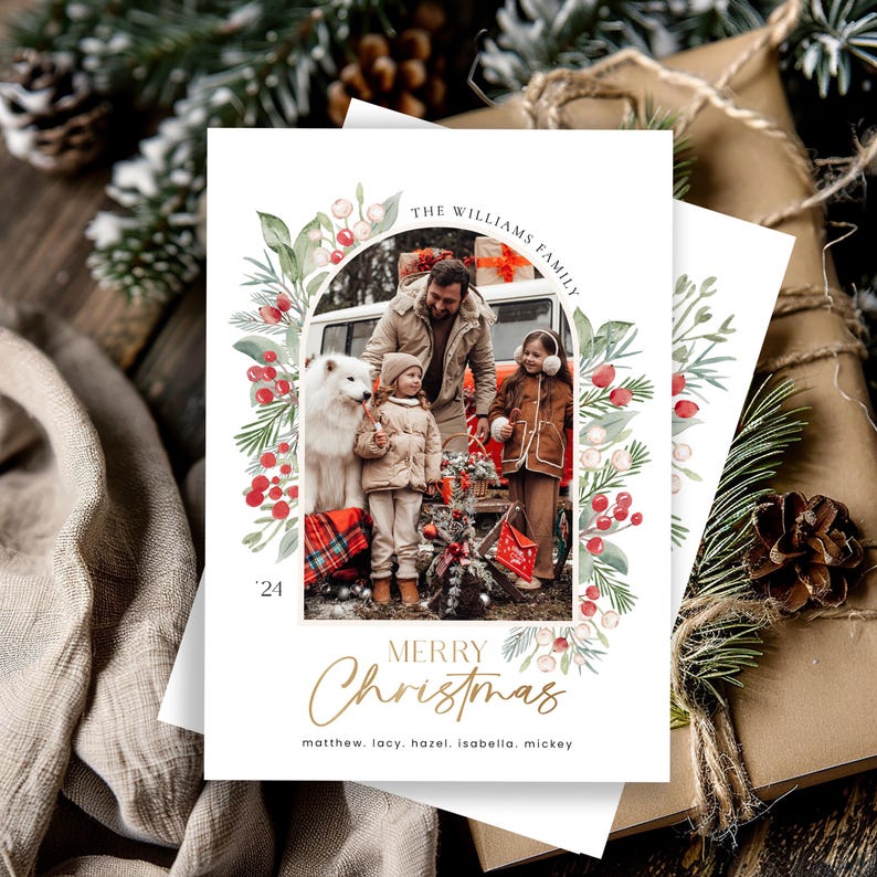 May include: A Christmas card featuring a family portrait with a white dog. The family is standing in front of a red car with a Christmas tree on top. The card has a watercolor border with red berries and green leaves. The text on the card reads "The Williams Family" and "Merry Christmas".