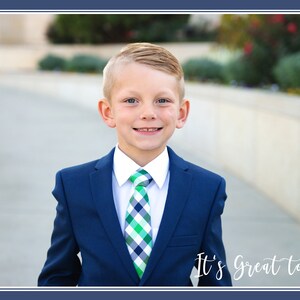 May include: A young boy wearing a blue suit with a white shirt and a green and white checkered tie. He is smiling and looking at the camera. The text "It's Great to be 8" is written in white cursive on the bottom right corner of the image.