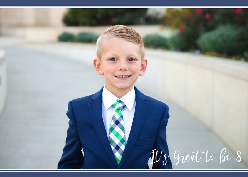 May include: A young boy wearing a blue suit with a white shirt and a green and white checkered tie. He is smiling and looking at the camera. The text "It's Great to be 8" is written in white cursive on the bottom right corner of the image.