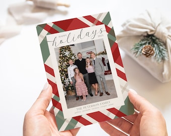 May include: A Christmas card with a red, white, and green plaid pattern. The card features a photo of a family standing in front of a Christmas tree. The text "Happy holidays 2021" is written in cursive at the top of the card. The text "The Peterson Family" is written below the photo, followed by the names "Jeffrey, Michelle, Zachary, Cooper, Annie".