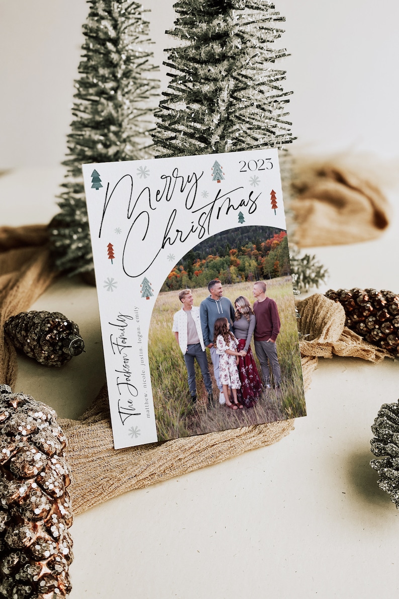 Pu&ograve; includere: Un biglietto di Natale bianco con una foto di una famiglia di cinque persone in piedi in un campo. Il biglietto ha un messaggio scritto a mano che dice "Buon Natale" e l'anno "2025". I nomi della famiglia sono elencati sotto la foto: "The Jockson Family: Matthew, Nicole, Justin, Logan, Emily."