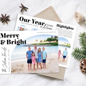 Puede incluir: Una tarjeta de Navidad con una familia de seis personas en una playa frente a una laguna tropical. La tarjeta tiene un fondo blanco con texto negro que dice "Merry & Bright" y "The Johnson Family". El texto "Our Year in Review 2022" tambi&eacute;n est&aacute; en la tarjeta.