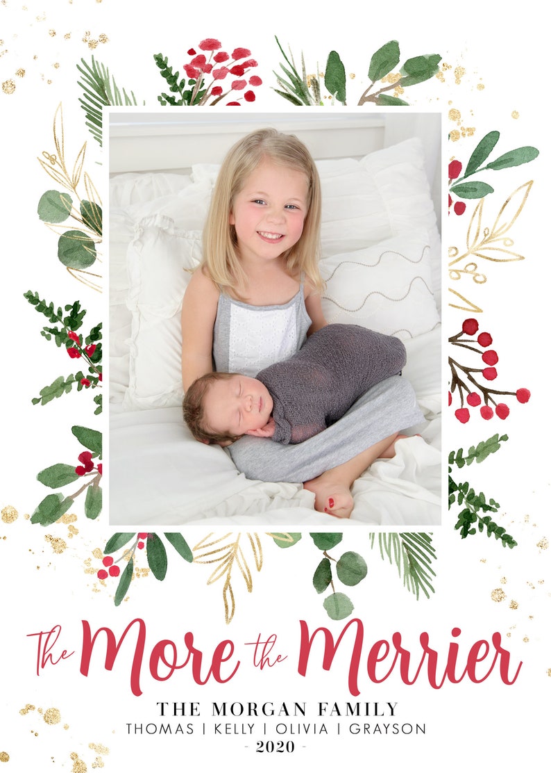 May include: A Christmas card featuring a watercolor illustration of greenery and red berries with gold accents. The card says "The More the Merrier" in red text and "THE MORGAN FAMILY THOMAS | KELLY | OLIVIA | GRAYSON - 2020 -" in black text. A photo of a young girl holding a baby is in the center of the card.