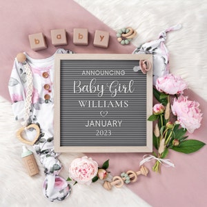 Puede incluir: Un tablero de letras con el texto "Announcing Baby Girl Williams" y un s&iacute;mbolo de coraz&oacute;n, seguido de "January 2023". El tablero est&aacute; rodeado de art&iacute;culos para beb&eacute;s de color rosa y blanco, incluyendo un mameluco, un chupete, un sonajero y flores.