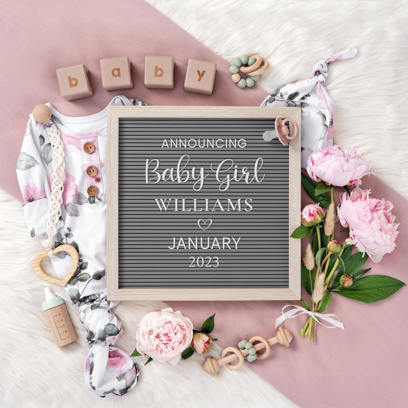 Puede incluir: Un tablero de letras con el texto "Announcing Baby Girl Williams" y un s&iacute;mbolo de coraz&oacute;n, seguido de "January 2023". El tablero est&aacute; rodeado de art&iacute;culos para beb&eacute;s de color rosa y blanco, incluyendo un mameluco, un chupete, un sonajero y flores.