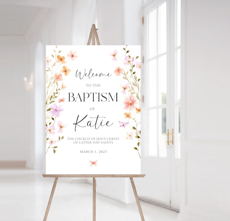 May include: A welcome sign for a baptism with a floral design in shades of pink and orange. The sign reads "Welcome to the Baptism of Katie The Church of Jesus Christ of Latter-day Saints March 1, 2025".