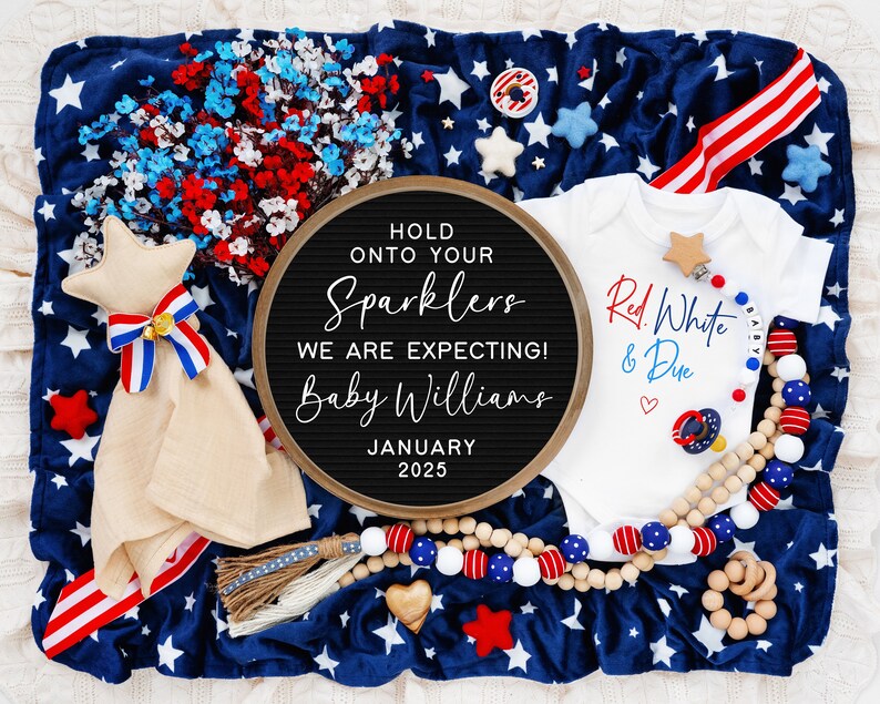 Op de afbeelding: Een zwart letterbord met de tekst "Hold onto your sparklers, we are expecting! Baby Williams, January 2025". Een wit rompertje met de tekst "Red, White & Due" en een rood hart. Een rood-wit-blauwe sterrendek met een stervormig knuffeldier.